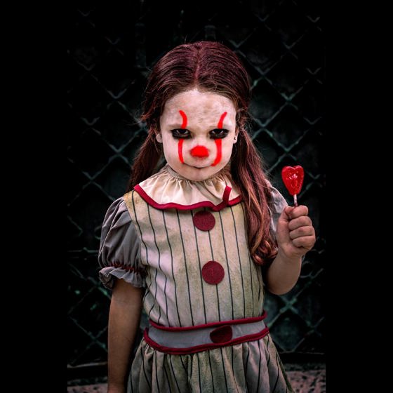 Lite flicka som håller i en godis klubba. Flickan är målad som en clown.