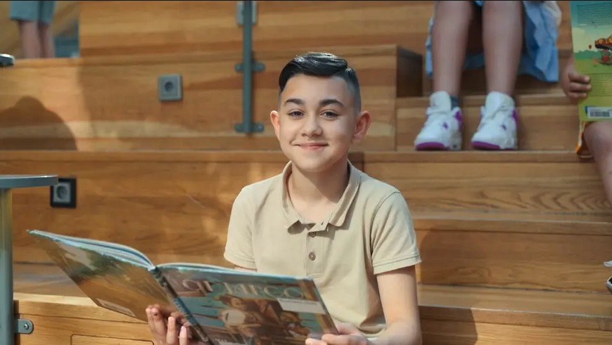 En pojke som sitter på en trapp och håller i en bok.