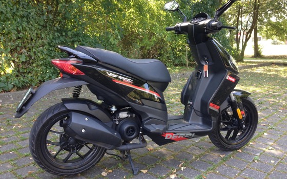 Svart och röd moped som står parkerad.