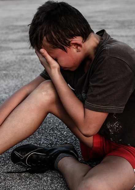 Barn som sitter på gruset och är ledsen. 