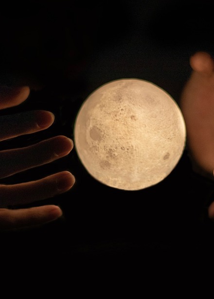 Händer som håller en svävande måne.