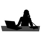 En person som sitter  vid en dator och pratar i telefon.