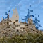 Ett slot som står längst upp på ett berg och skog nedanför.