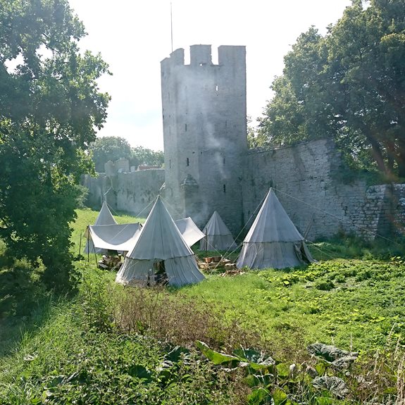 Tre vita tält framför en slottsmur.